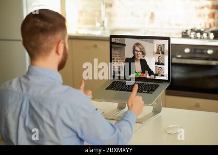 Rückansicht eines männlichen Mitarbeiters, der per Fernzugriff Berichte seiner Kollegen über ein Unternehmen durch eine Videokonferenz auf einem Laptop-Computer zu Hause abhört. Stockfoto
