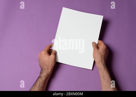 Männliche Hände hält einen geschlossenen dreifach-Katalog mit leerem Cover auf lila Hintergrund, Mock-up-Serie Vorlage bereit für Ihr Design, Cover-Auswahl pat Stockfoto