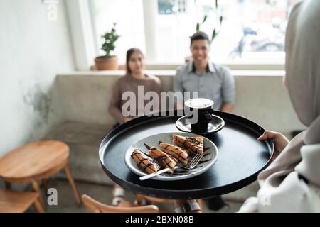 Ein Glas Kaffee und Toast auf einem Tablett wird von einem Kellner für ein paar Café-Kunden serviert Stockfoto