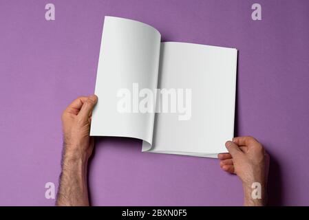 Männliche Hände halten einen geöffneten Buch-Katalog mit leeren Seiten auf lila Hintergrund, Mock-up-Serie Vorlage bereit für Ihr Design, Seiten Auswahlpfad i Stockfoto