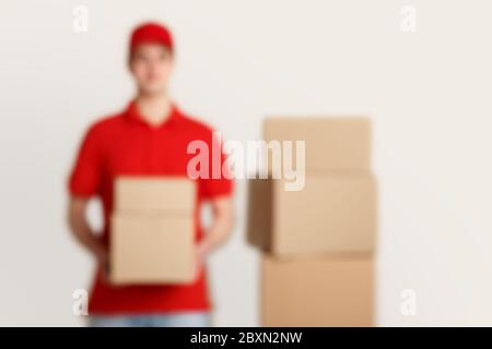Verschwommenes Foto des Kuriers in roter Uniform, hält Pakete, in der Nähe Stapel von Kisten Stockfoto