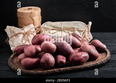 Rote Kartoffeln auf dunklem Holzhintergrund. Konzept für die Lebensmittelzustellung, umweltfreundliche Verpackung. Platz zum Kopieren, Nahaufnahme Stockfoto