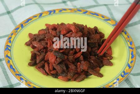 Beerenobst, Goji-Beeren, Wolfberries oder Lycium Barbarum Früchte in gelber Schale mit Essstäbchen. Eine gute Quelle für Vitamin C, A, Zink, Eisen und Antioxi Stockfoto