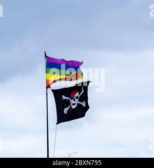 Flags. Jolly Roger alias Skull and Crossbones und Regenbogen. Gegen Himmel, ungewöhnliche Gegenüberstellung. Stockfoto