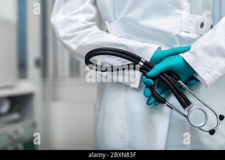 Arzthand in einem weißen Mantel Nahaufnahme hält ein Phonendoskop auf dem Hintergrund eines Krankenhauszimmers. Raum kopieren, Medizinkonzept Stockfoto