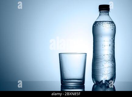 Plastikflasche mit Mineralwasser mit leerem sauberen Becher oder Glas neben in einem niedrigen Winkel Seitenansicht mit Copyspace Stockfoto