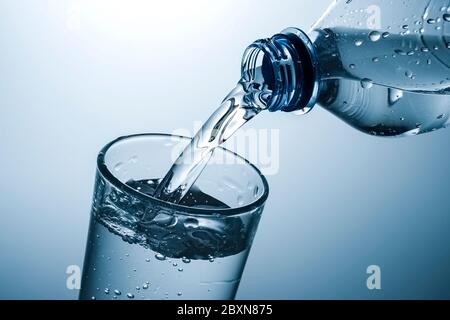 In einem großen Glas wird in einem Nahbereich am Hals der Plastikflasche und am Rand des Tumblers Wasser gegossen Stockfoto
