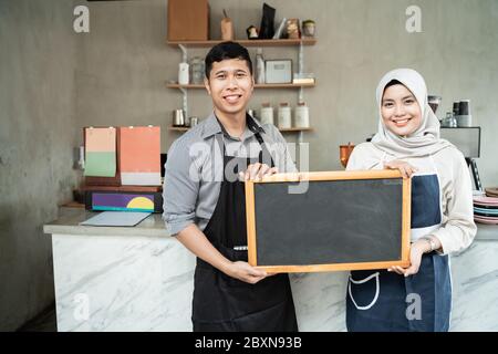 Paar Kellnerin stehend halten eine Tafel in einem Kaffeehaus von Coffee-Shop Hintergrund Stockfoto