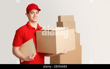 Kurier und Paket im Lager. Liefermann, der Box und Tablet in der Nähe von Paketstapeln hält Stockfoto