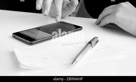 Schwarz-Weiß-Bild von Frau, die finanzielle Berechnung auf dem Smartphone vor der Unterzeichnung Bankscheck Stockfoto