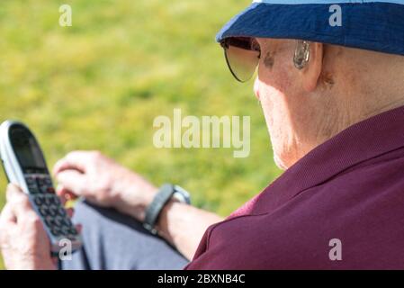 An ihrem Geburtstag, tragen Sonnenbrille und einen Sommerhut, sitzen draußen in der Sonne in ihrem Garten, genießen einen Fernruf von ihrer Enkelin. Stockfoto