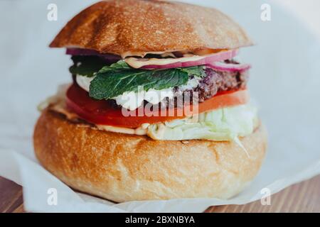 Köstliche frische hausgemachte Käse Burger mit gegrilltem Fleisch, Käse, Tomaten, Salat und Zwiebelringe in Kraftpapier. Stockfoto