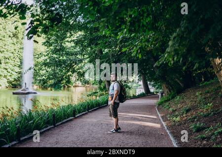 Sofia Park, Uman. Schöner Mann mit Bart und Rucksack auf einer Park-Tour. Ein Mann in einem T-Shirt und Shorts geht entlang der See-Böschung mit einem Brunnen Stockfoto