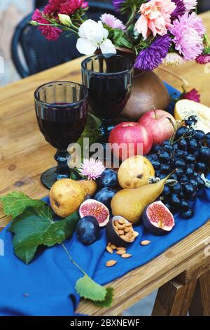 Stillleben mit verschiedenen Früchten und einem Blumenstrauß in einer Vase auf der blauen Tischdecke..Weingläser, Trauben, Äpfel, Birnen, Feigen und Astern. Stockfoto