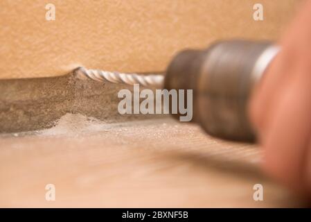 Die Hand hält den Bohrer in der Nähe der Wand, Nahaufnahme, das Thema der Reparatur und Gebäude Stockfoto