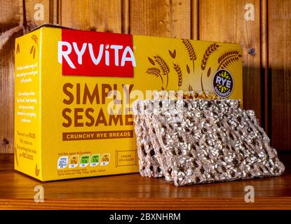 Eine Schachtel Ryvita ‘simpliziert Sesam’ knusprige Roggenbrote, mit vier der hochfaserigen knusprigen Brote, die sich gegen die Schachtel lehnen, auf einem Regal in einem Kiefernschrank. Stockfoto