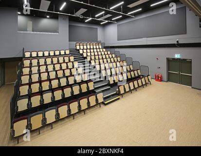 Ausziehbare Bleacher-Sitzmöbel in einer neu erbauten Schulhalle im Süden Londons, Großbritannien. Zeigt das System vollständig ausgefahren und bietet 9 Reihen gestufter Sitzplätze. Stockfoto