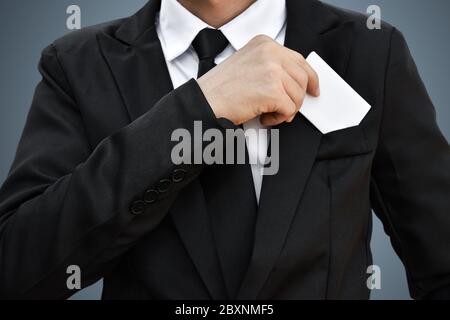 Nahaufnahme von Geschäftsmann, der aus der Tasche weißes Stück Papier in schwarzen Anzug nimmt. Idee für Business-Kreditkarte oder Visitenkarte. Stockfoto