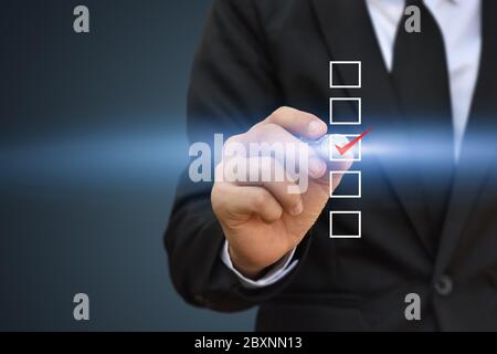 Geschäftsmann Schreiben roten Häkchen in einem Kontrollkästchen auf blauem Hintergrund. Stockfoto
