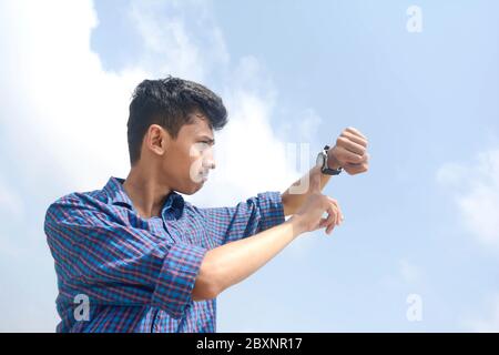Porträt eines jungen Mannes, der auf seine Uhr schaut. Isoliert auf dem Hintergrund des Himmels. Stockfoto
