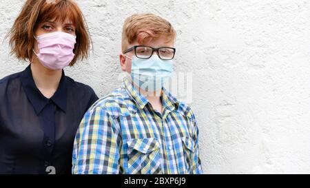 Junge rothaarige Frau und Junge mit einer chirurgischen Maske stehen vor einem Wandhintergrund. Stockfoto