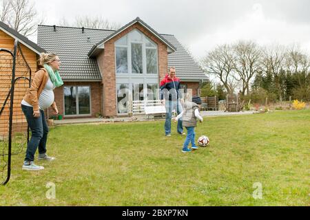 Eine Familie spielt im Garten hinter dem Haus mit einem Fussball Stockfoto