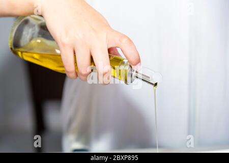 Nahaufnahme einer weiblichen Hand, die einen Olivenölspender hält, aus dem Öl auf einem unscharf darüberströmenden Hintergrund ausgießt. Gesundes Essen Konzept. Stockfoto