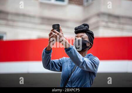Frau, die ein Kopftuch und eine Gesichtsmaske trägt, hält ein Mobiltelefon hoch, um Demonstranten der BLM UK zu Filmen. Park Lane, London, England, Großbritannien Stockfoto