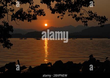 Sonnenuntergang am Westsee (Xi Hu) in Hangzhou, Provinz Zhejiang, China. Blick auf den West Lake in Hangzhou bei Sonnenuntergang mit einem orangen Licht über dem See. Stockfoto