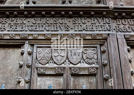 Detail der geschnitzten Schilde und lateinischen Inschrift auf der Oak Tür des Norman Bogen von Tewkesbury Abbey, Gloucestershire, England Stockfoto