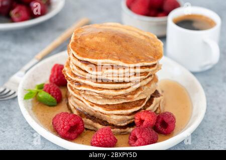 Pfannkuchen mit Sirup und Himbeeren auf dem Teller, Tasse Espresso auf dem Hintergrund. Leckeres süßes Frühstück Stockfoto