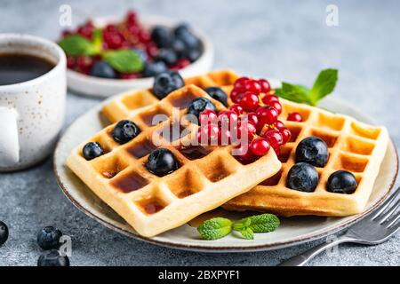 Belgische Waffeln mit Beeren und einer Tasse Kaffee auf dem Teller, Nahaufnahme. Leckeres süßes Frühstück Stockfoto