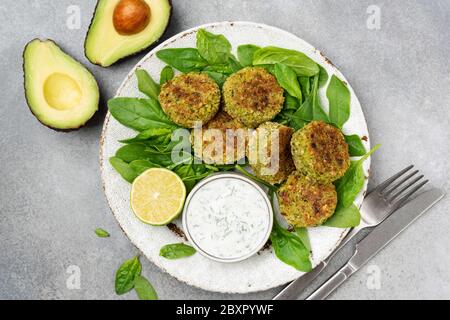 Falafel mit Spinat serviert mit griechischem Joghurt Tsatziki-Sauce auf grauem Beton Textur Hintergrund. Draufsicht. Gesunde vegetarische Vorspeise, arabische Küche Stockfoto