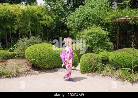 Japanischer Kimono auf europäischem Mädchen.kleines europäisches Mädchen in japanischem Kimono in japanischem kleinem Garten. Stockfoto