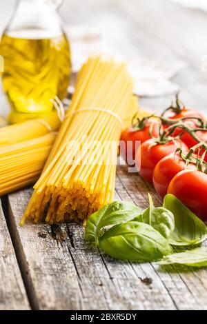 Rohe Spaghetti-Pasta, Kirschtomaten, Basilikumblätter und Olivenöl auf Holztisch. Stockfoto