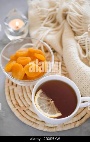 Still life Details im Interieur der Wohnzimmer. Tasse Tee und getrocknete Aprikosen auf einem Tisch, Kerzen und knited Decke. Gemütliche Stimmung im Herbst oder Winter i Stockfoto