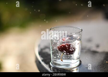 Rote Kirsche fallen in ein Glas Wasser produzieren Wasser Spritzer, frieren in der Zeit Foto, konzeptionell. Stockfoto