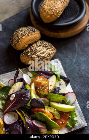 Köstlicher Salat aus Tomaten und Guacamole, mit grünem Apfel und Rettich, verziert mit Leinsamen, auf dunklem Hintergrund Stockfoto