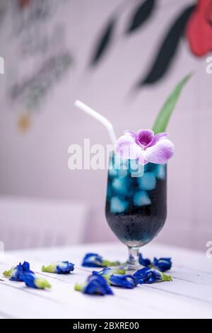 Schmetterlingserbsenschmuck auf einem Tisch aus pastellrosa Holz vor der Zementwand im Freien mit lila Orchidee und Pandan-Blatt. Stockfoto