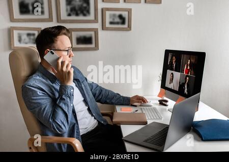 Junger Mann, der von zu Hause aus Papierkram macht, während er Laptop benutzt und das Telefon in der Hand hält. Stockfoto