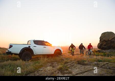Freunde Radfahrer Enduro-Bikes in den Bergen vor dem Pickup Off Road Truck bei warmem Herbstuntergang. MTB Abenteuer und Autoreisen concep Stockfoto