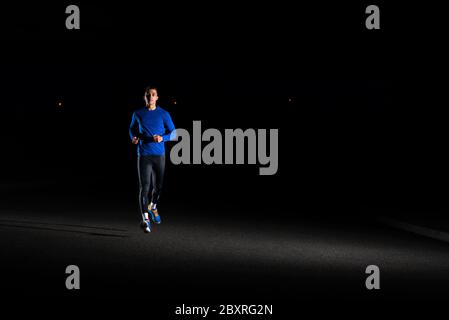 Junger Mann in Blau läuft nachts draußen. Urban Running. Gesundes Lifestyle- und Sportkonzept. Stockfoto