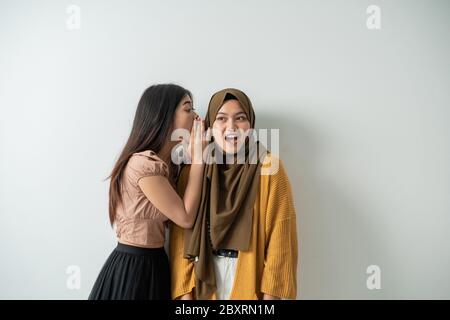 Das junge Mädchen flüsterte ihrem Freund mit einem überraschten Ausdruck einen isolierten Hintergrund ins Ohr Stockfoto