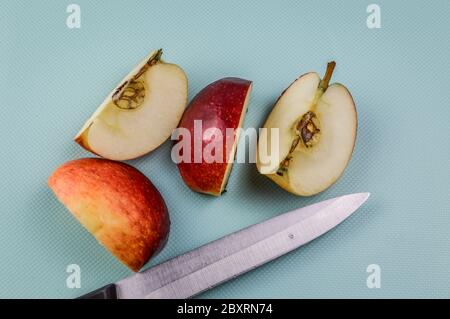 Viertel eines roten Bio-Apfel mit Küchenmesser auf einem hellblauen strukturierten Hintergrund geschnitten Stockfoto