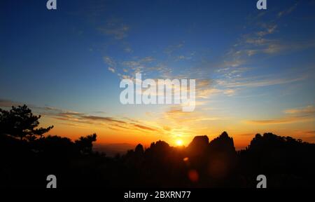 Berg Huangshan in der Provinz Anhui, China. Sonnenaufgang über Huangshan mit einem bunten Himmel, Wolken und Silhouette des Berges. Mit Streulicht. Stockfoto