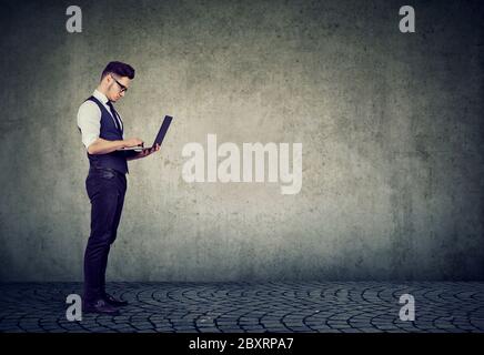 Junger Mann stehend mit Laptop-Computer Stockfoto