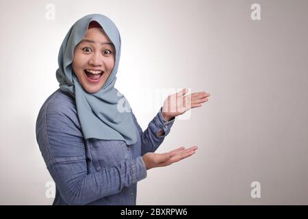 Porträt einer jungen asiatischen glücklichen muslimischen Frau, die lächelt und auf eine Präsentation von etwas auf ihrer Seite zeigt, mit Kopierraum Stockfoto