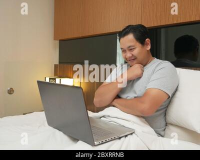 Portrait des jungen asiatischen Mann mit Laptop auf dem Bett, erfolgreiche männliche Unternehmer arbeiten Online-Geschäft von zu Hause, glücklich lächelnd Ausdruck Blick auf l Stockfoto
