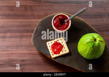 Salz- und Wassercracker, Schüssel mit Guava-Marmelade und Guava-Scheibe auf rustikaler Steinstruktur. Stockfoto