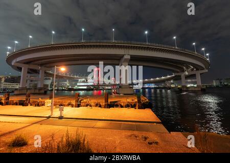 Nachtansicht der Regenbogenbrücke, rot beleuchtet als Zeichen für 'Tokyo Alert (Coronavirus Alert für Tokyo Area)' in Odaiba, Japan. Stockfoto